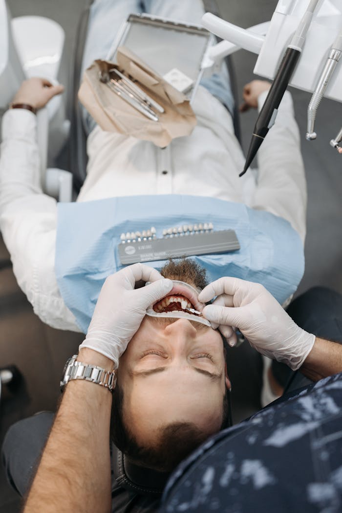 A dentist conducts a dental exam on a male patient lying in a dental chair indoors.